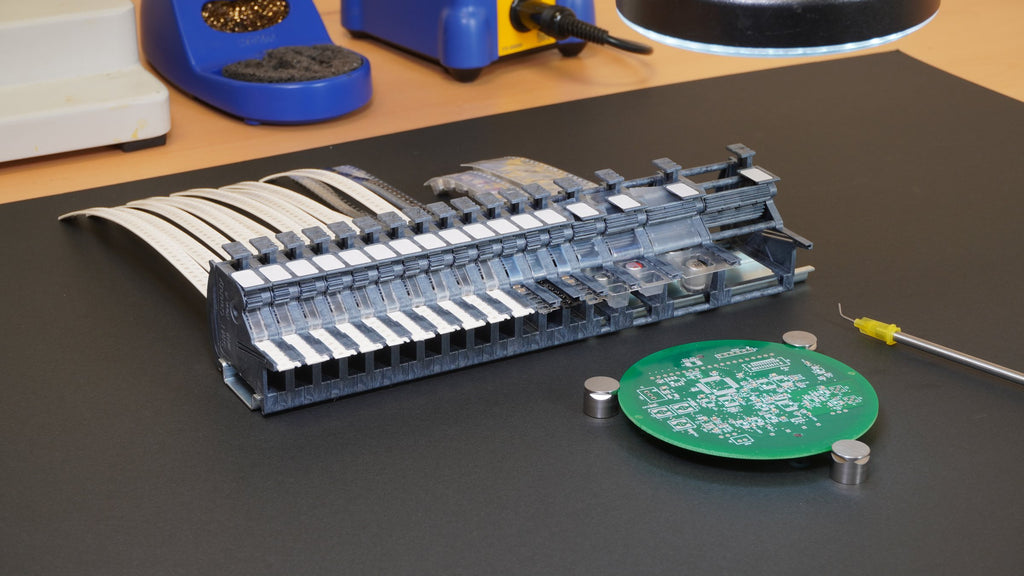MTI feeder bank on a workbench beside a PCB held by magnets, with a vacuum pickup tool and soldering station