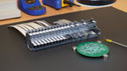 MTI feeder bank on a workbench beside a PCB held by magnets, with a vacuum pickup tool and soldering station