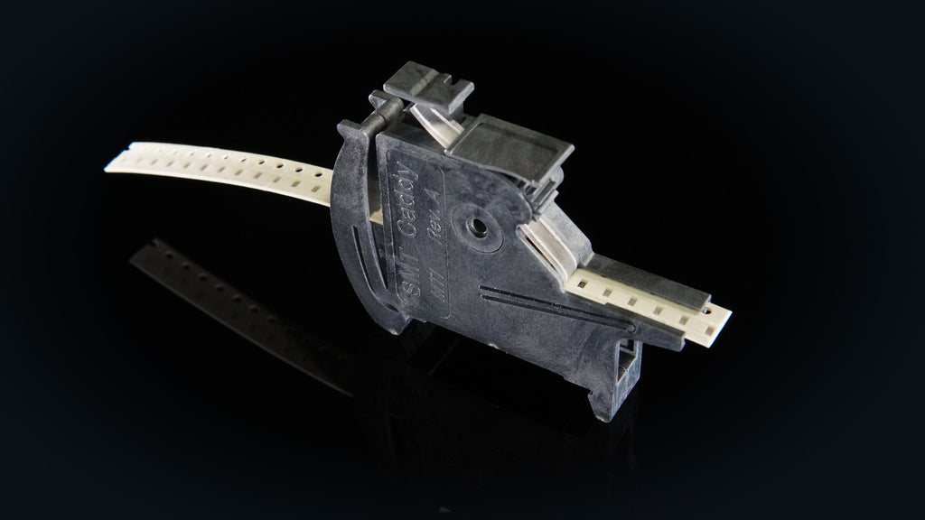 SMT Caddy MTI tape feeder loaded with 8 mm paper tape, on a dark reflective surface